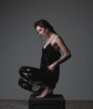 Woman in a black dress sitting on a reflective surface with a dark background
