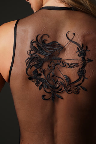 A black temporary tattoo of a female archer with floral details applied to a woman's upper back, shown from behind.