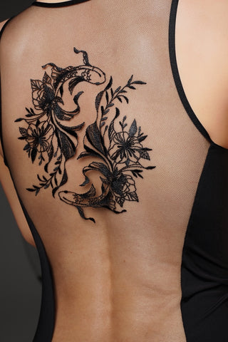 A black floral and snake temporary tattoo applied on the back of a person wearing a black mesh backless top.