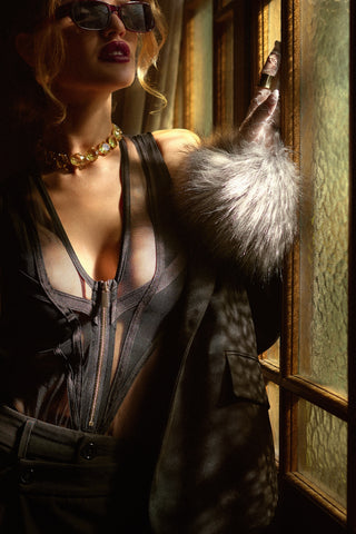 Woman in a dark outfit with fur accents with her hand on a blurred glass window