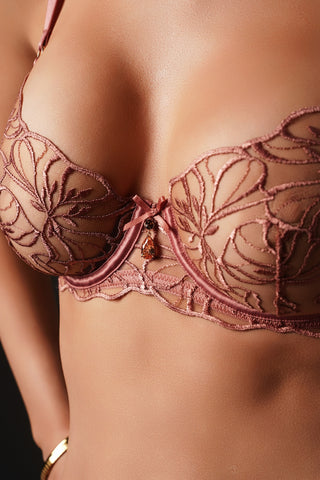 Close-up of a model wearing a dusty rose lace bra with floral embroidery and a small amber gem accent at the center front.