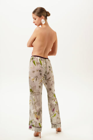 Back of a woman wearing floral printed silk pajama pants on a white background