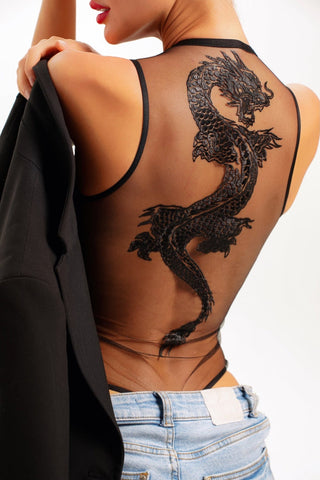 Woman wearing a lingerie bodysuit string with a tattoo like embroidered dragon with jeans and holding a blazer on the side