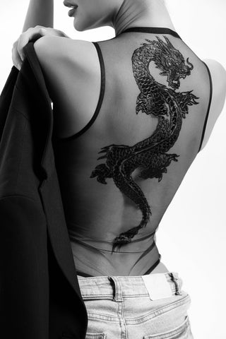 Person with a detailed dragon tattoo on their back, wearing a dark top and light pants.