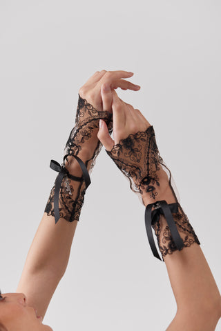 Black lace gloves with bow details on a neutral background